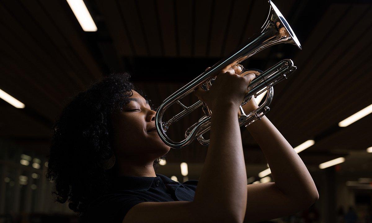 Woman holding a trumpet smiles at the camera.