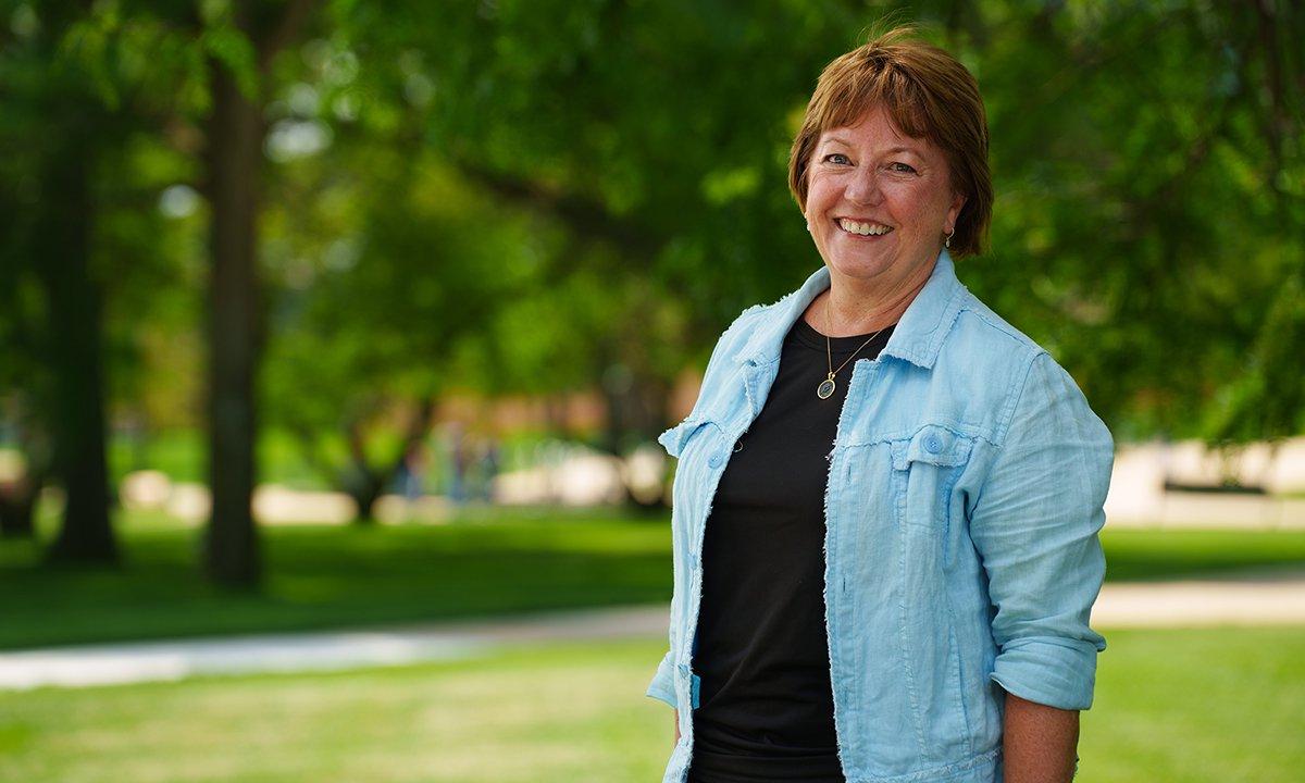 Beth Talbert stands smiling outside on O U campus.